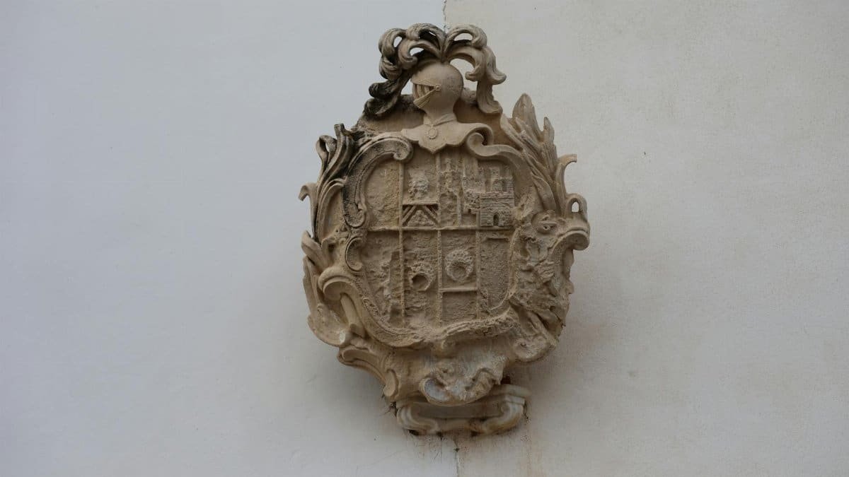 Detailed stone heraldry plaque featuring intricate designs on a white wall in Puerto Real, Andalucía, Spain.