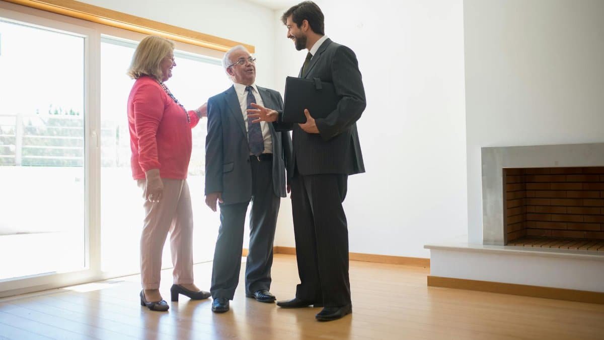 A real estate agent shows an empty house to senior clients, highlighting the spacious room.
