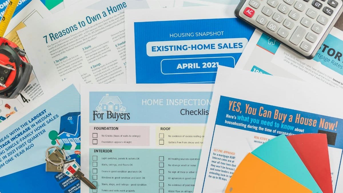 Flat lay of real estate brochures, checklists, and a calculator for home buying.