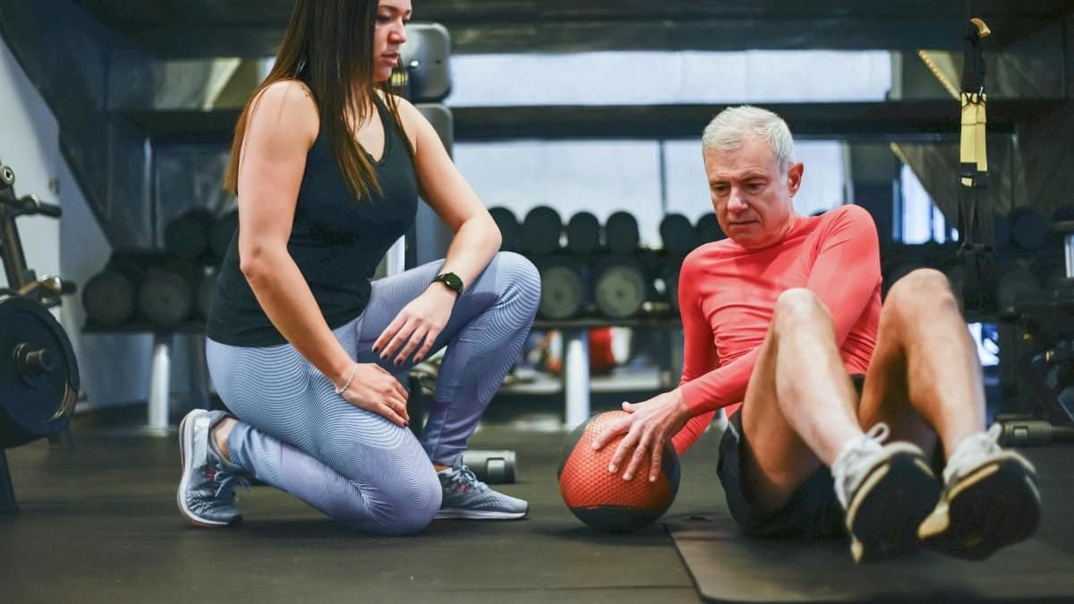A senior man exercising with a personal trainer in a gym, focusing on core workouts.