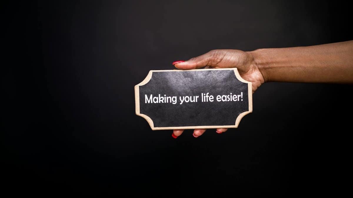 A hand holding a sign with the quote 'Making your life easier!' against a black background.