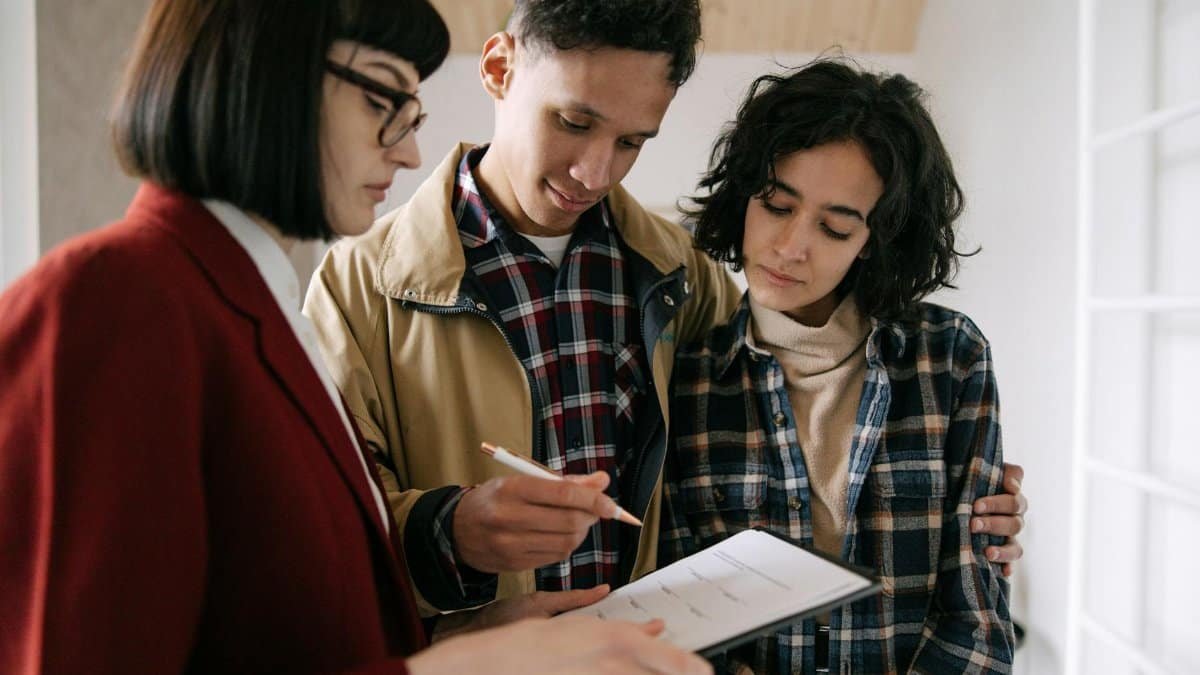 A young couple consults with a real estate agent about documents inside an apartment.