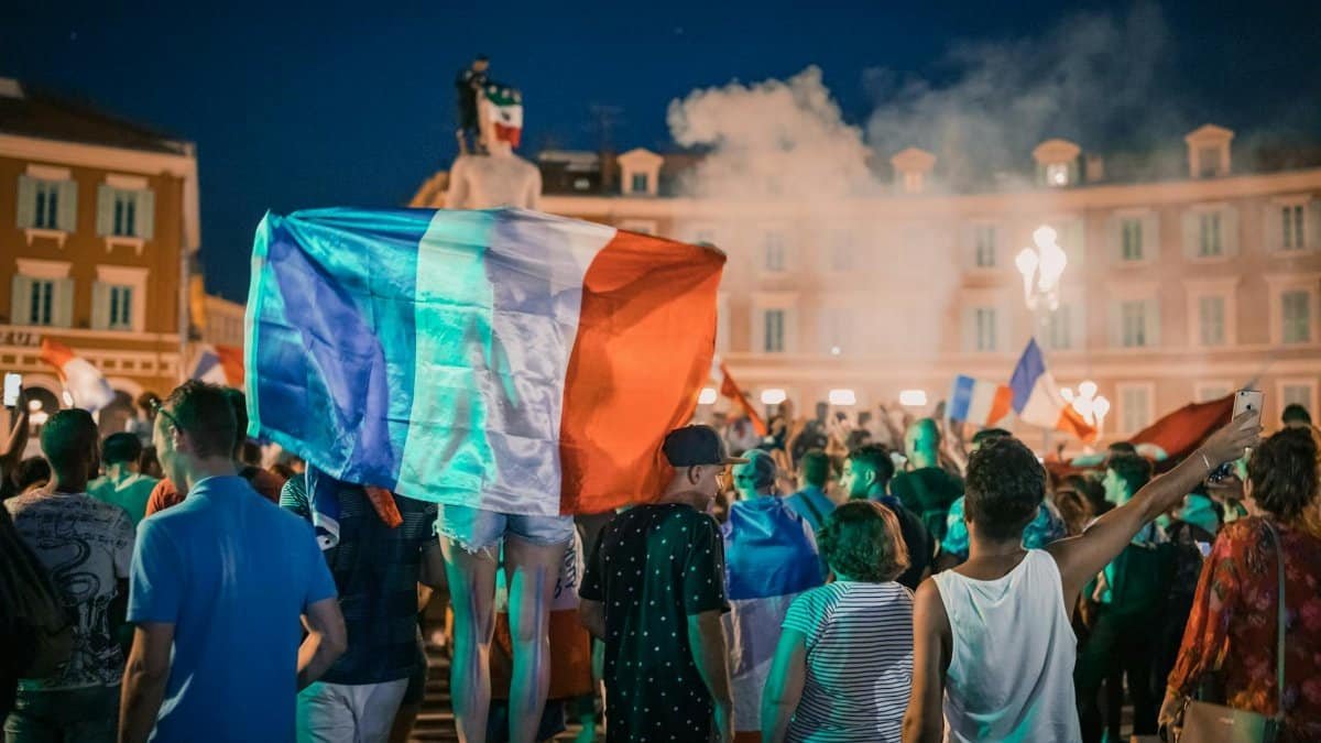 Vivid night-time celebration in France with crowds waving flags in city square.