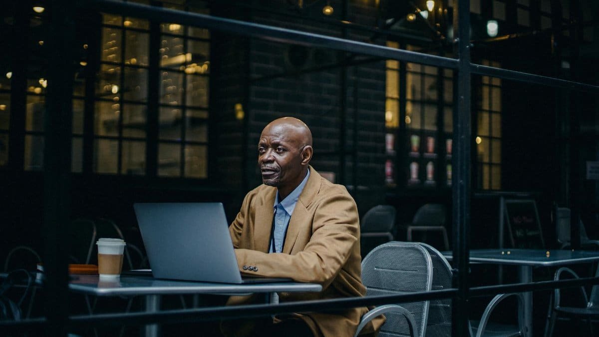 African American man in a cafe working on laptop, enjoying a coffee, warm ambiance.