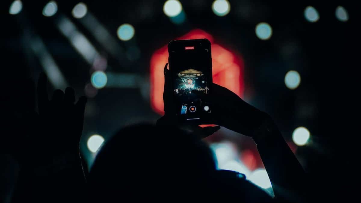 Silhouette using a smartphone to record a live concert scene.