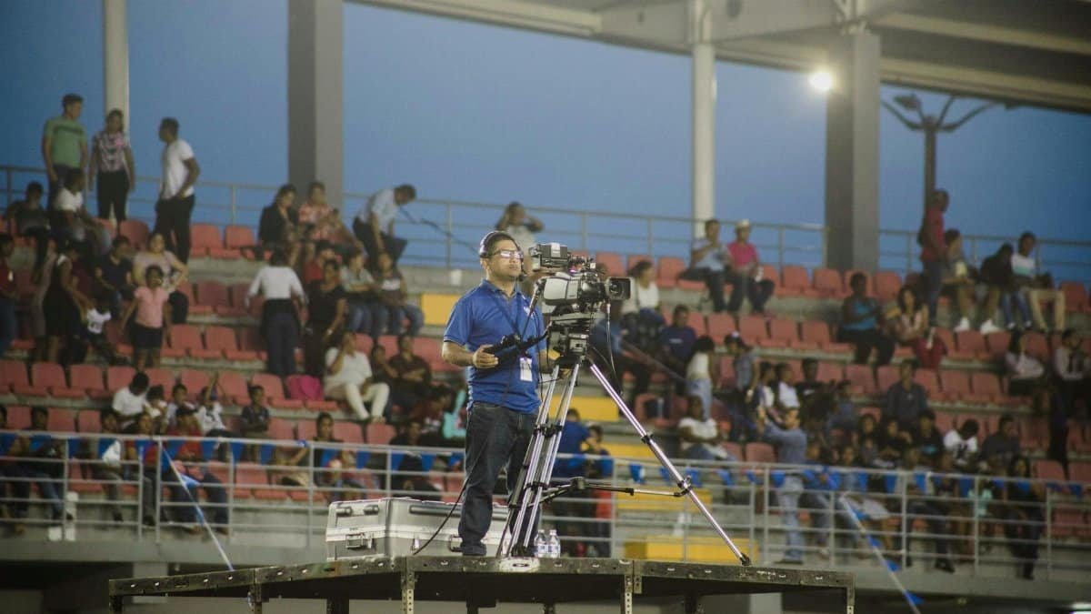 Cameraman on platform capturing footage at crowded stadium event.
