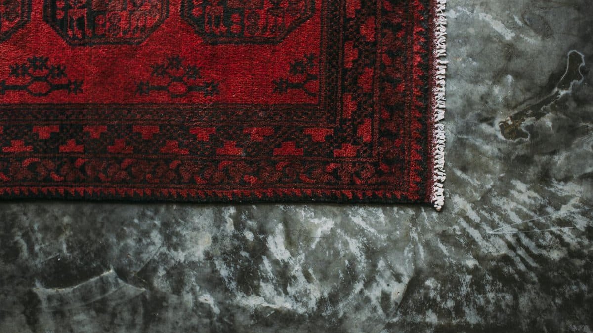 Close-up of a red floral patterned carpet on a textured concrete floor.