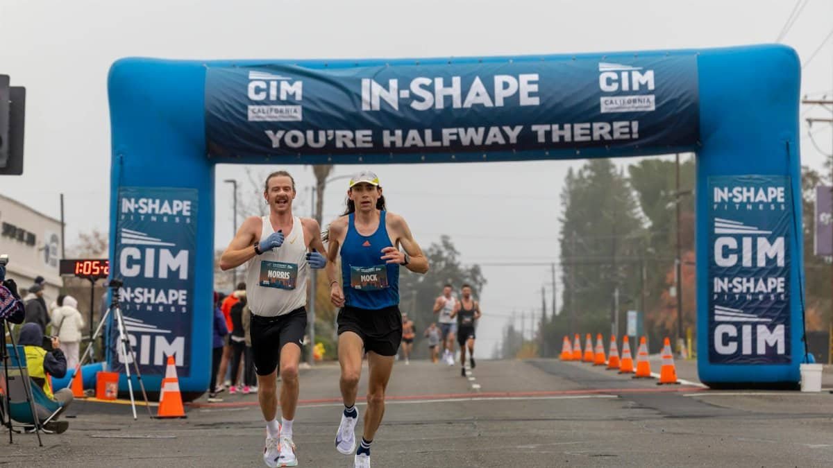 Two marathon runners competing in a foggy race reach the halfway mark under a blue archway.