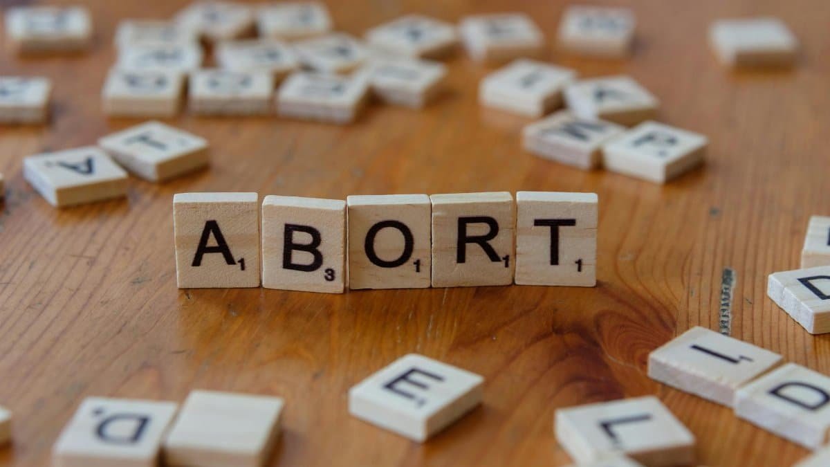Scrabble tiles spell the word 'abort' on a wooden table, sparking discussion.