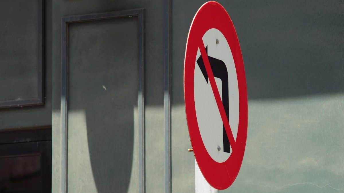 A no left turn road sign displayed prominently in an urban setting against a building background.