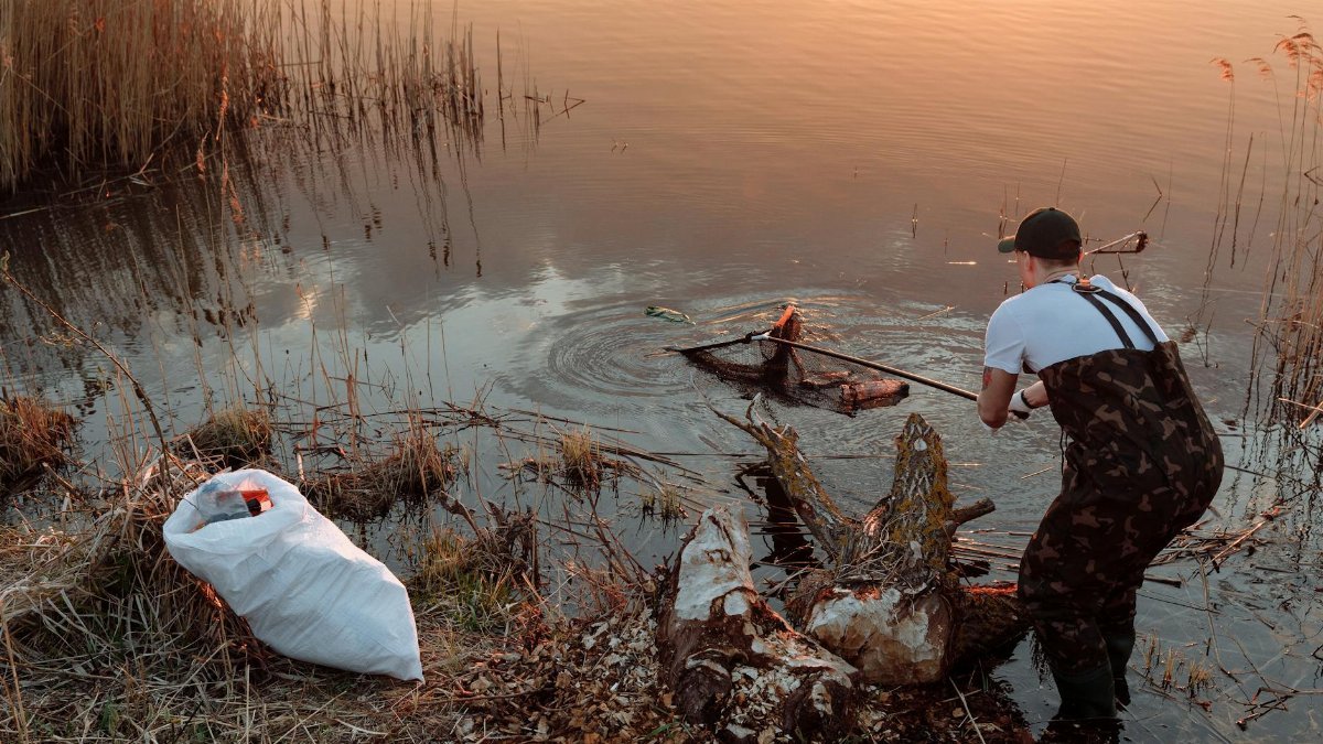 Man cleaning lake banks using a net, promoting environmental conservation.