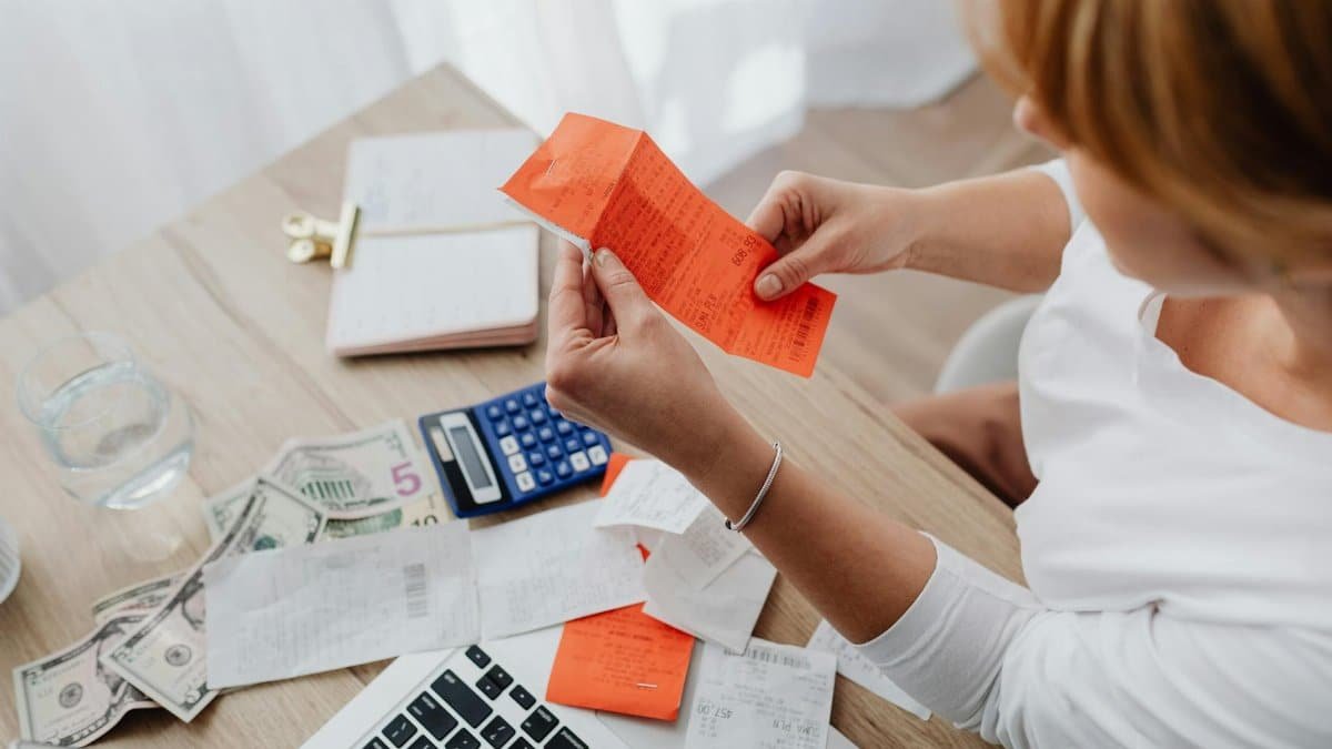 Woman using calculator and receipts at home office desk for finance management.