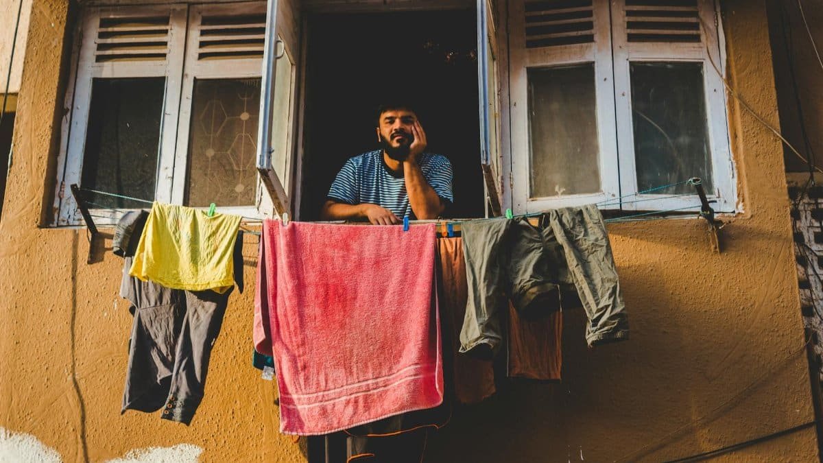 A man leaning out of a window with colorful laundry hanging outside, capturing city life.