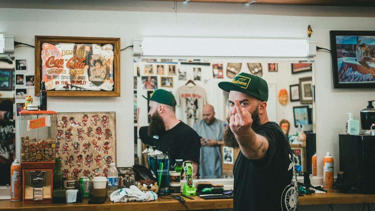 A bearded man makes a rude gesture in a vintage barber shop setting.
