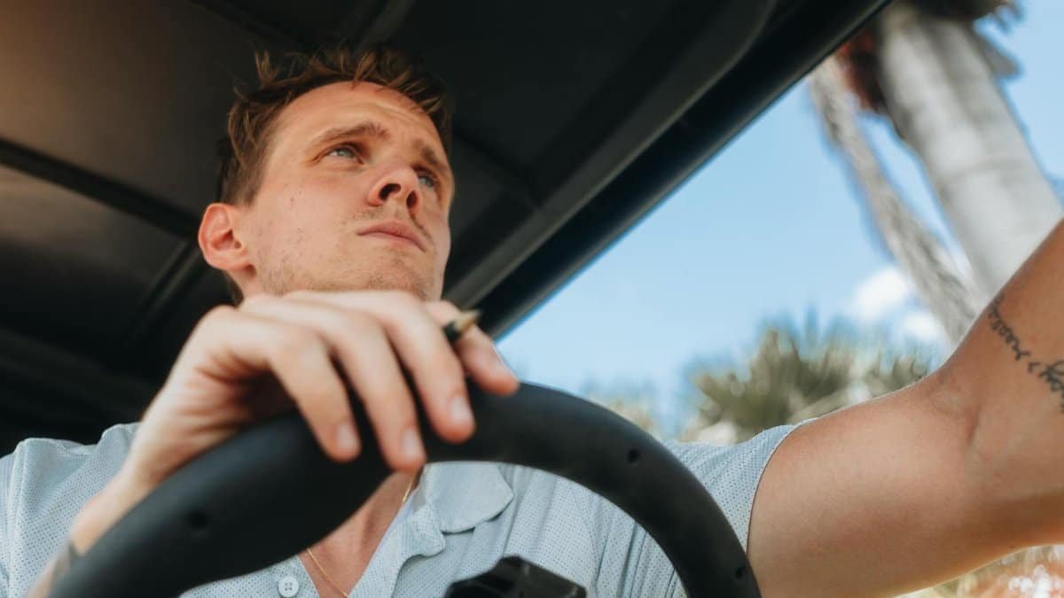 Young man confidently steering a golf cart under clear blue skies.