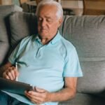 Elderly man using a tablet on a sofa, enjoying leisure time at home.