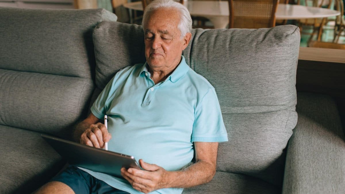 Elderly man using a tablet on a sofa, enjoying leisure time at home.