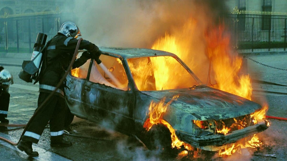 Firefighters extinguish a burning car in an urban setting, showcasing emergency response