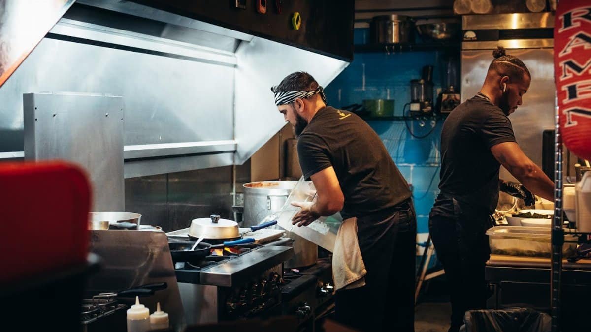 Two chefs preparing meals in a bustling restaurant kitchen, focused on culinary tasks.