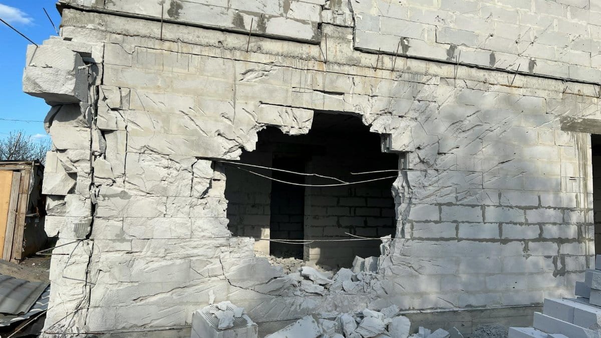 Concrete building wall with a large hole, showing damage and rubble, under a clear blue sky.