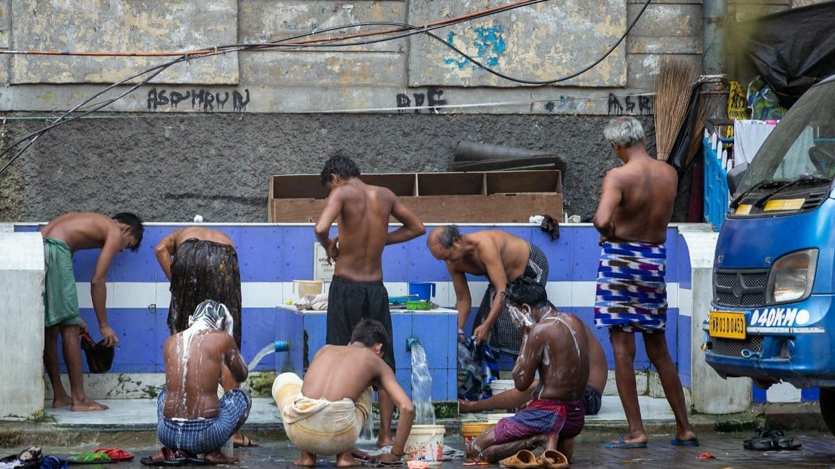 Men bathing outdoors, washing at a communal area in a city setting.