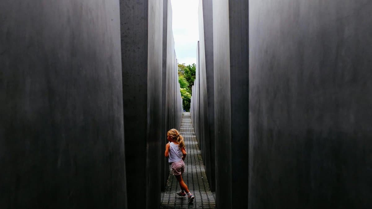 A young girl runs playfully through the narrow pathways of a modern concrete monument.