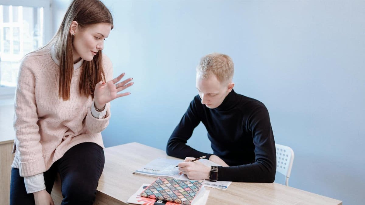 Female tutor helping male student with homework at a desk indoors.