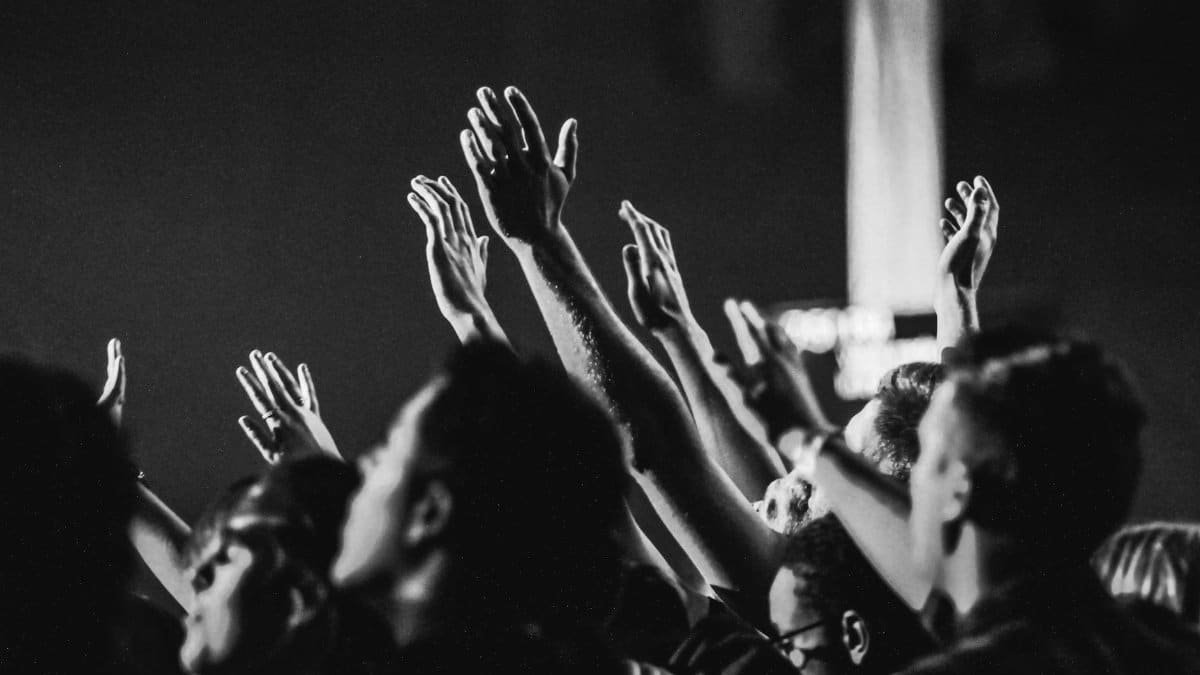 Dynamic black and white photo of a concert audience with hands raised, capturing the energy of live music.