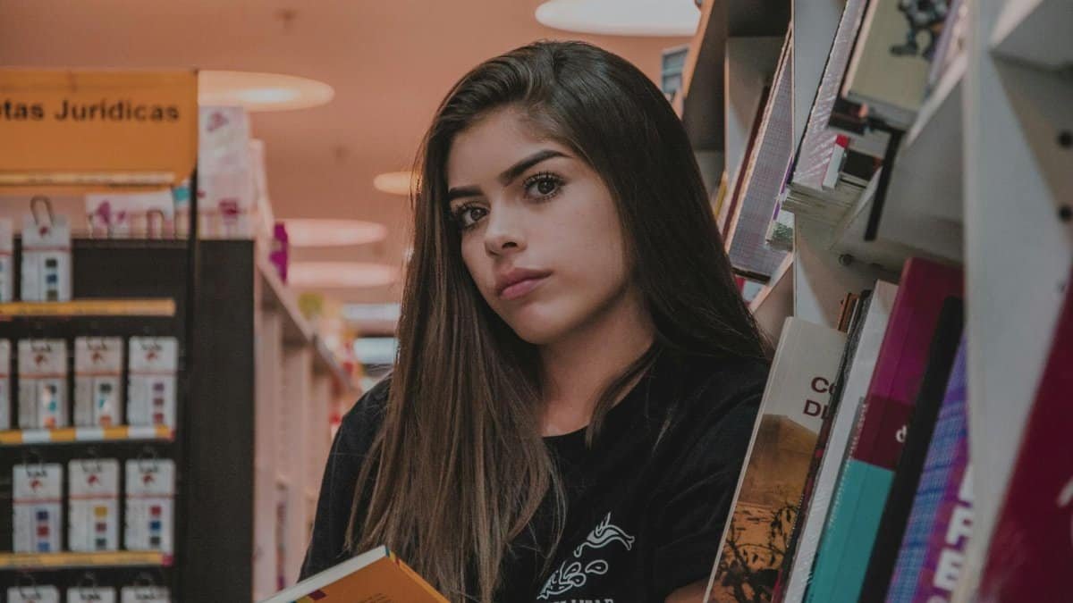 A young woman with long hair reading a book in a cozy bookstore aisle.