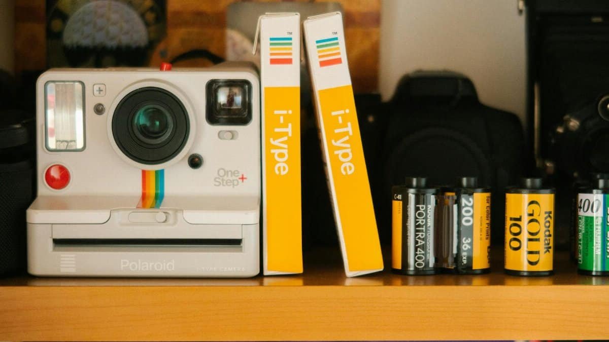 A classic Polaroid OneStep Plus camera with film rolls on a wooden shelf, showcasing retro photography equipment.