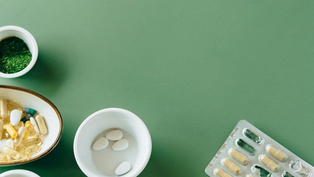 A flat lay of assorted pills and herbs on a green background emphasizing natural health remedies.