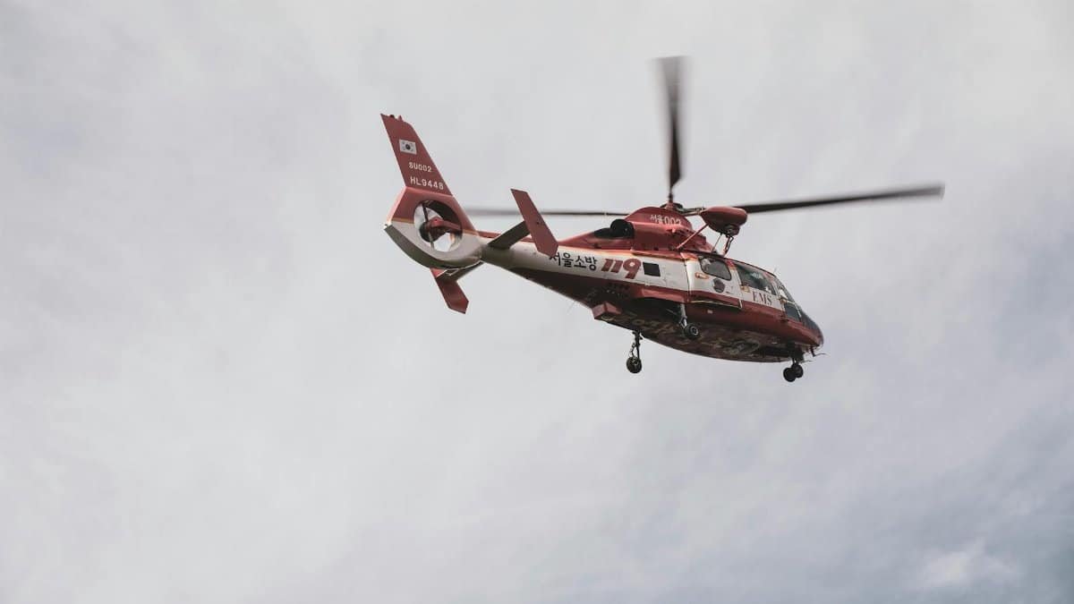 Red and white emergency helicopter flying in a cloudy sky.