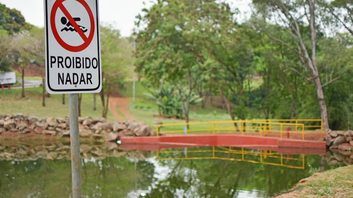 Proibido Nadar sign by a reflective pond in a lush park setting emphasizing safety.