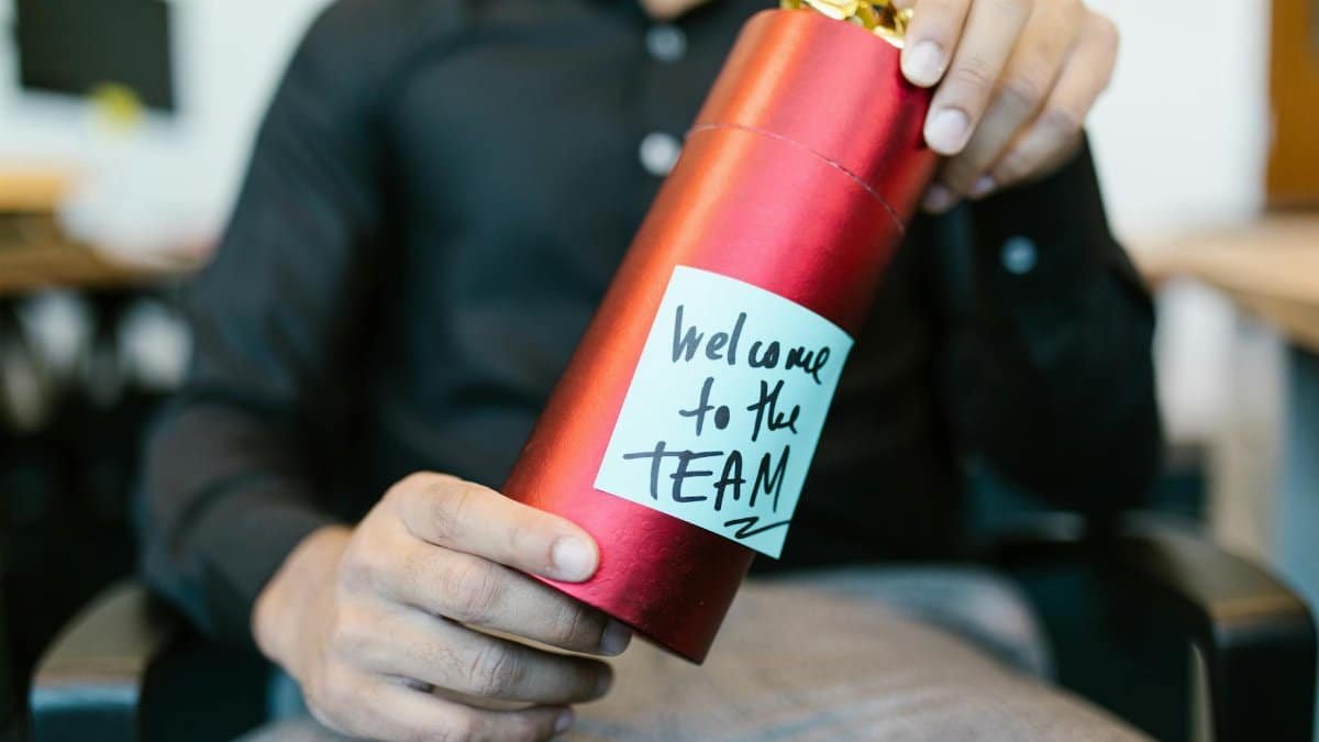 A red gift box held by a person with a welcome to the team note, ideal for new hire announcements.