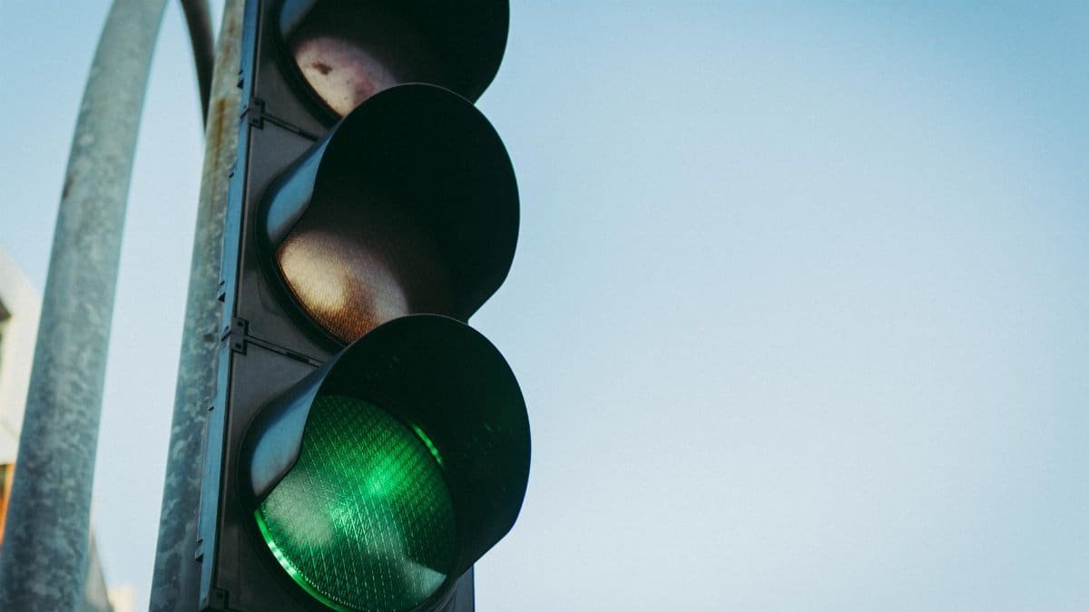 Close-up of a green traffic light against a clear blue sky, symbolizing go and safety.