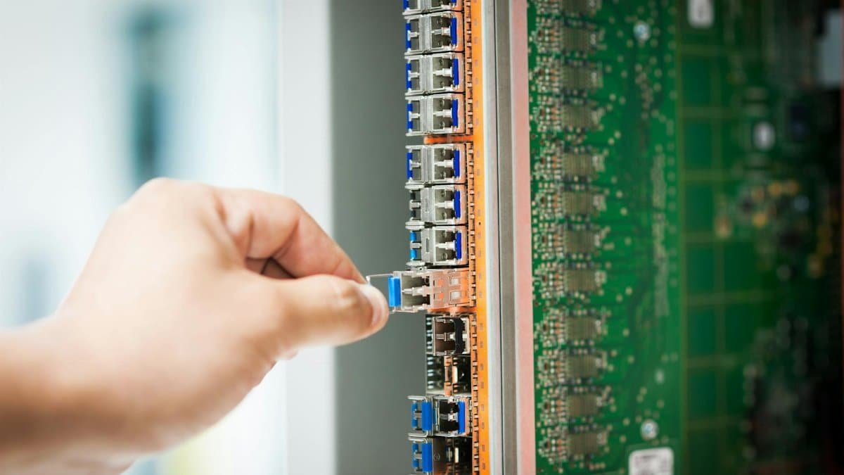 An individual connecting a cable into a network server port indoors, focusing on technology setup.