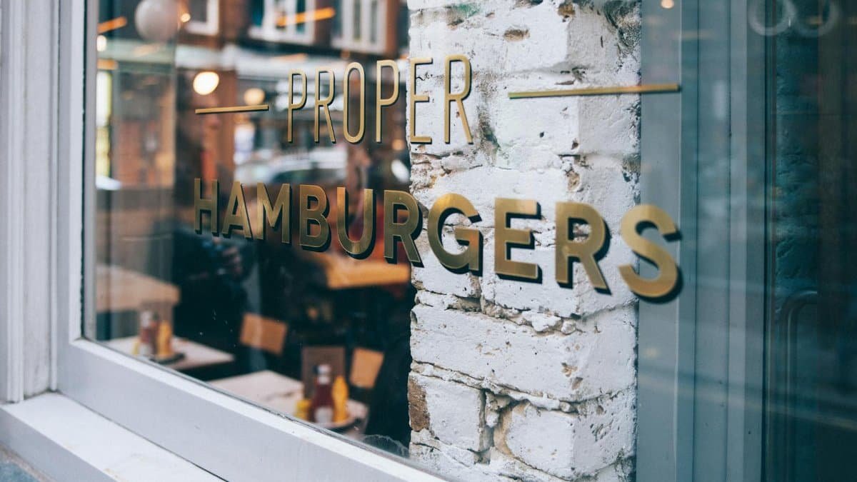 Contemporary restaurant facade with reflective glass windows displaying 'Proper Hamburgers'.