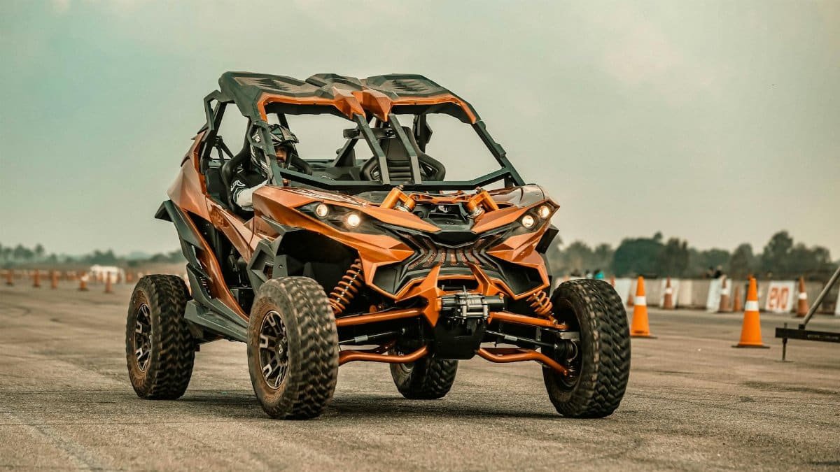 A striking orange off-road buggy navigating an asphalt track with safety cones in the background.
