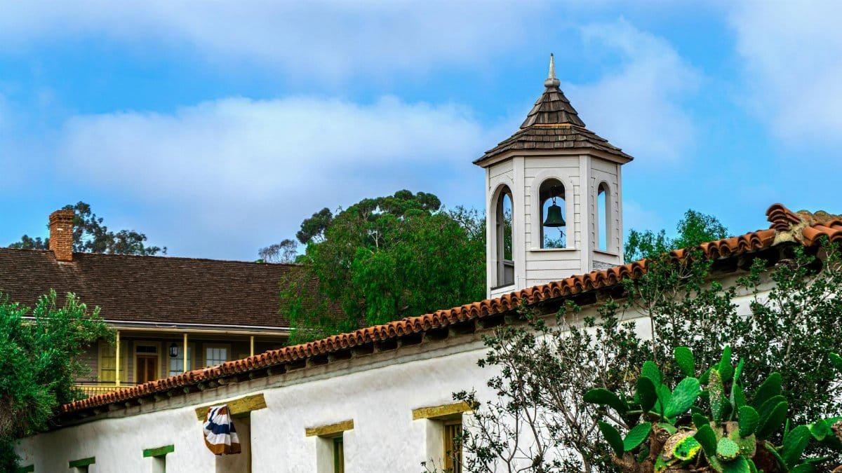 A picturesque view of a historic mission bell tower surrounded by lush greenery in San Diego, CA.