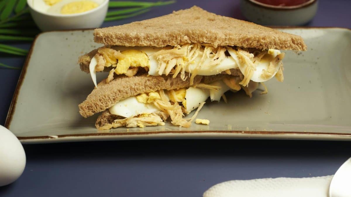 Close-up of a wholesome egg salad sandwich served on a ceramic plate, featuring whole wheat bread and garnished with slices of boiled egg.