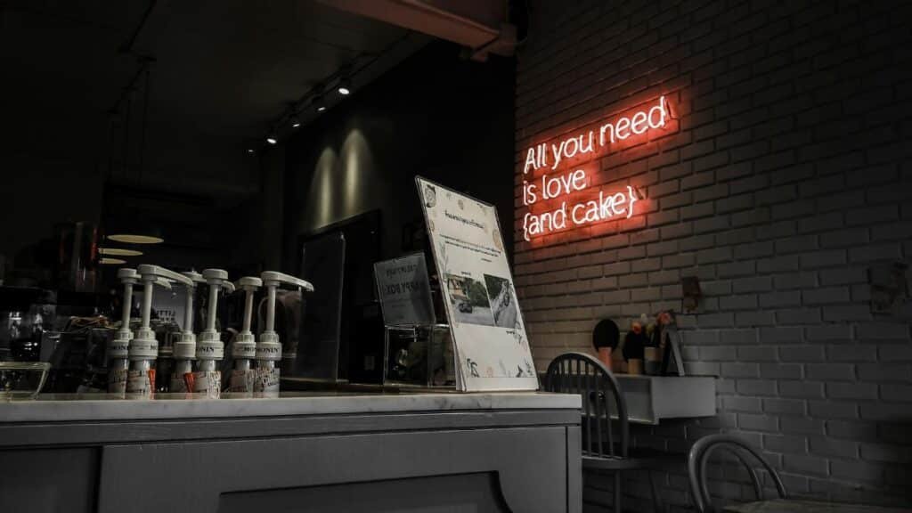 Intimate cafe setting with a neon sign reading 'All you need is love (and cake)'