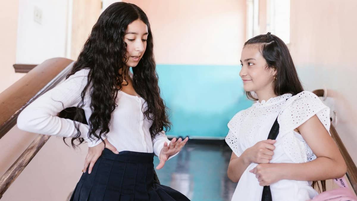 Two teenage girls talking and bonding on a school staircase.