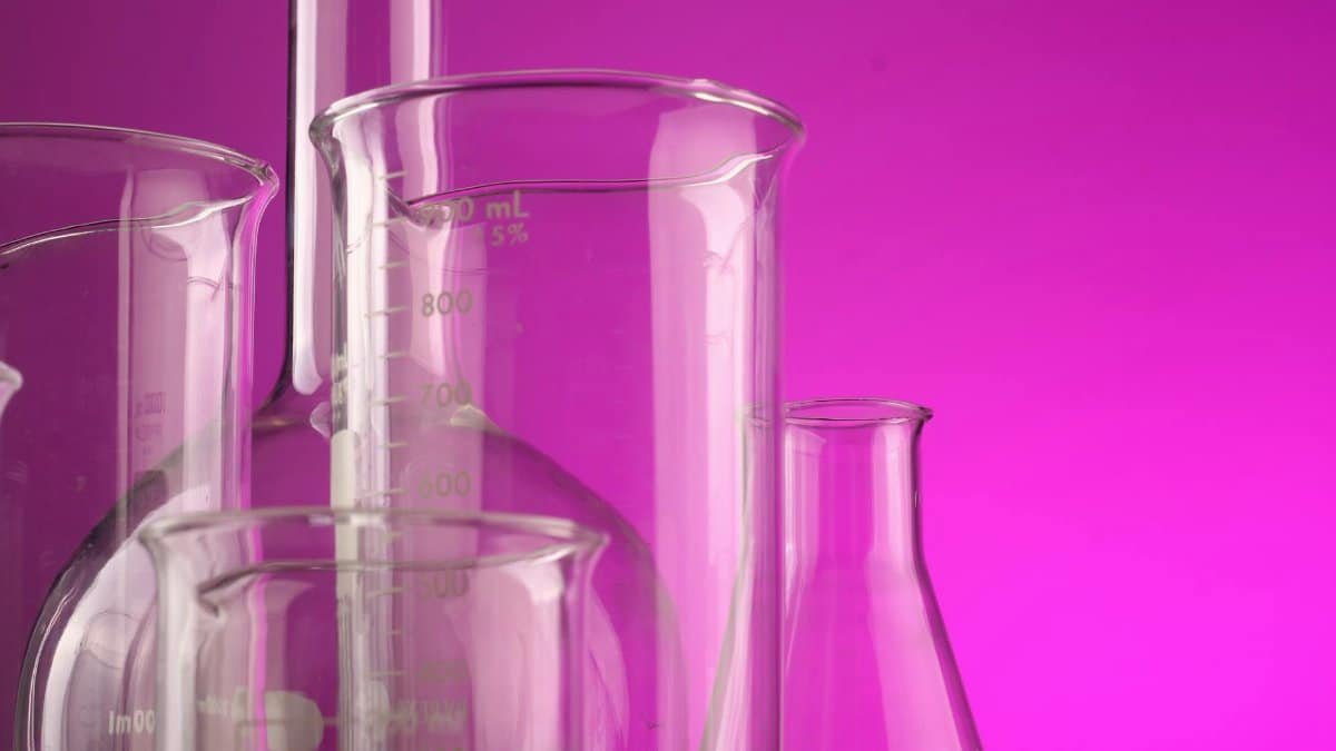 Clear glass laboratory flasks with volume measurements against a vibrant purple backdrop, ideal for science themes.
