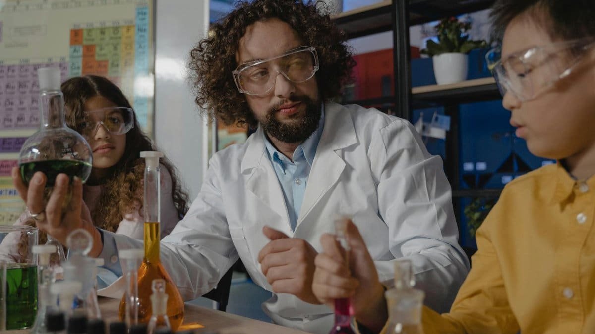 Students and teacher conducting a colorful science experiment using lab glassware in a classroom setting.