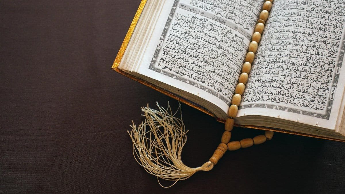 A Quran open to Arabic text with prayer beads resting on a brown surface, symbolizing Islamic faith.