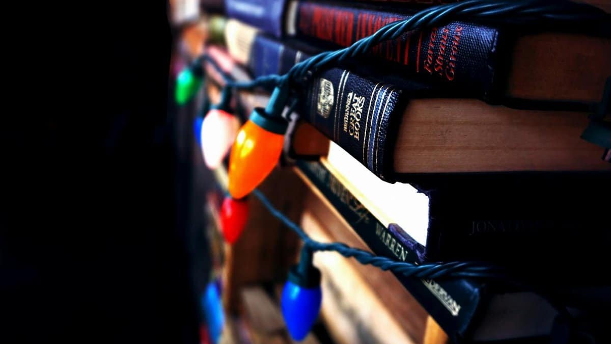 Close-up of books wrapped with colorful Christmas lights, a cozy indoor scene.