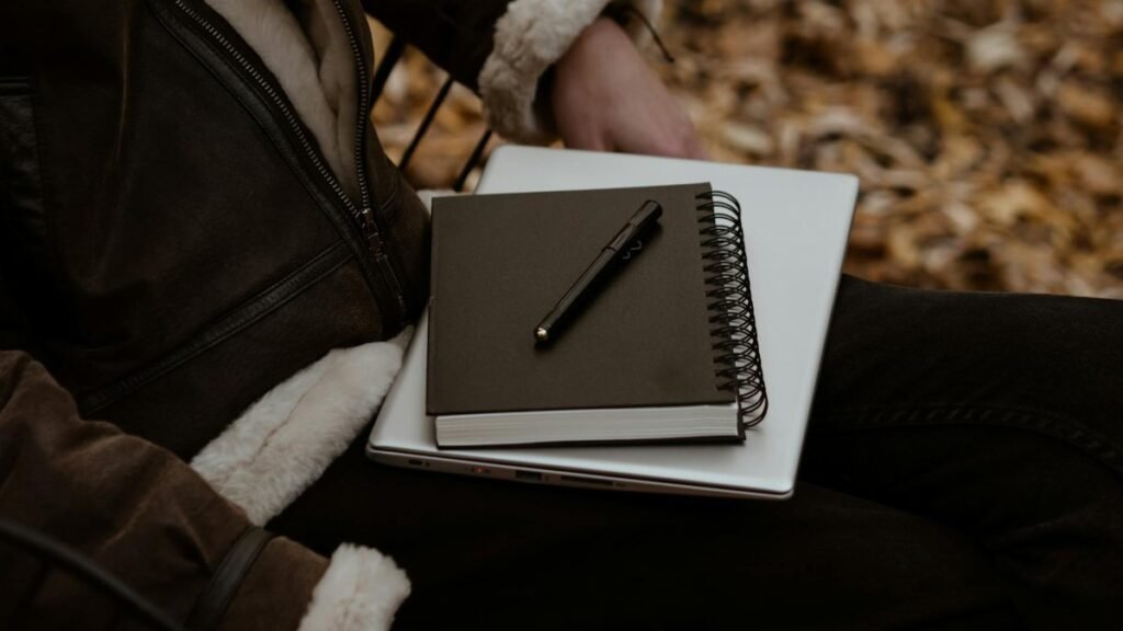 A person sitting outdoors with a notebook and laptop, surrounded by autumn leaves, representing a cozy work setup.