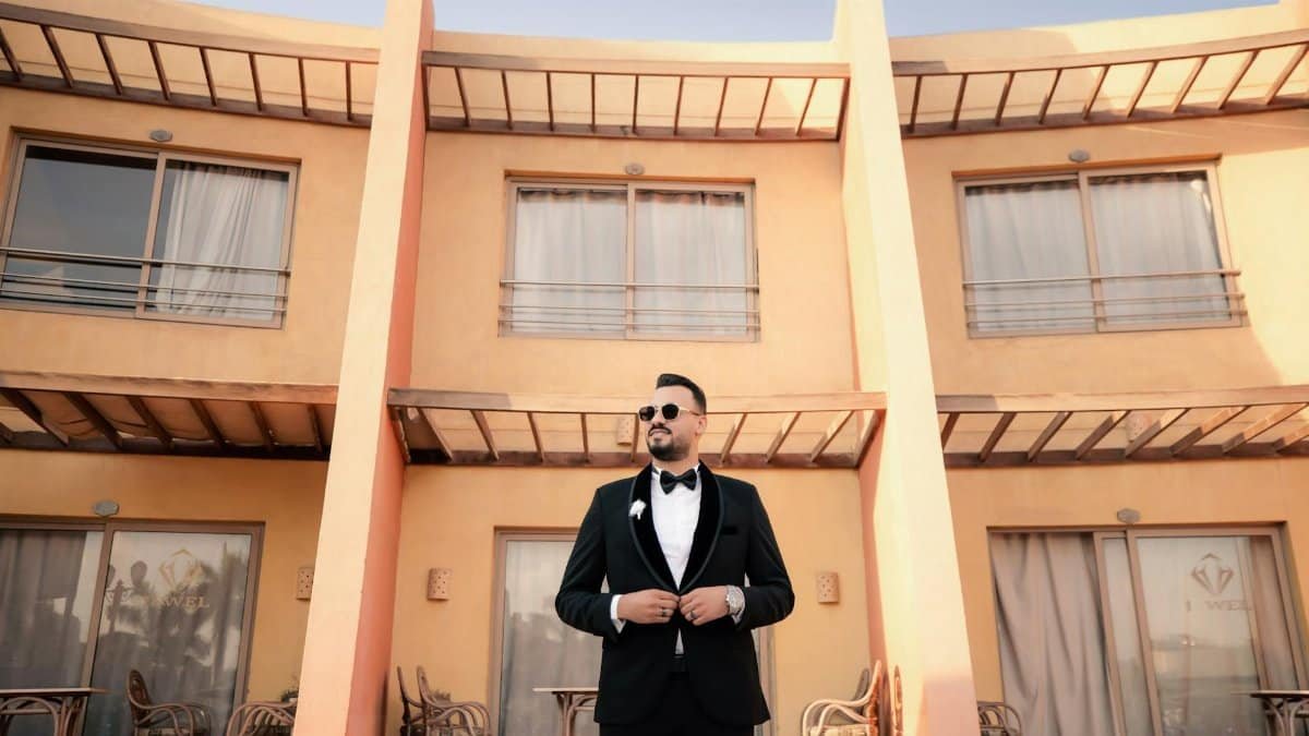 Stylish groom in sunglasses stands confidently in front of modern architecture.