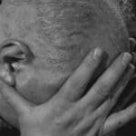 A close-up of an elderly man in black and white showing deep emotion and sadness.
