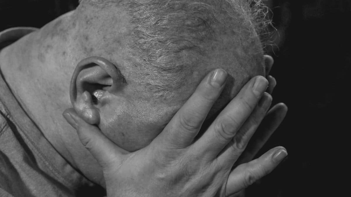 A close-up of an elderly man in black and white showing deep emotion and sadness.